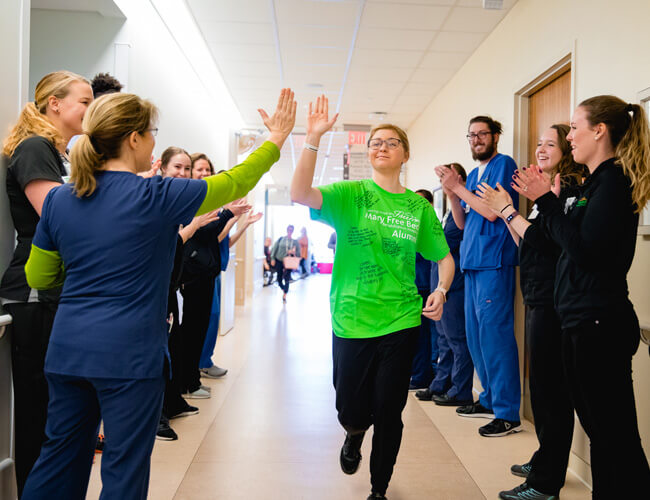 Lauren Ziegler high-fiving staff members in the hallway of Mary Free Bed during her rehabilitation.