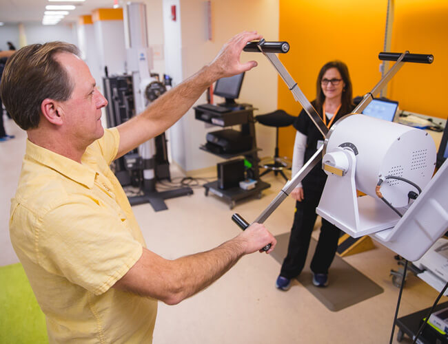 A patient engages in graded exposure therapy using specialized equipment at Mary Free Bed Pain Rehabilitation Center, supervised by a therapist.
