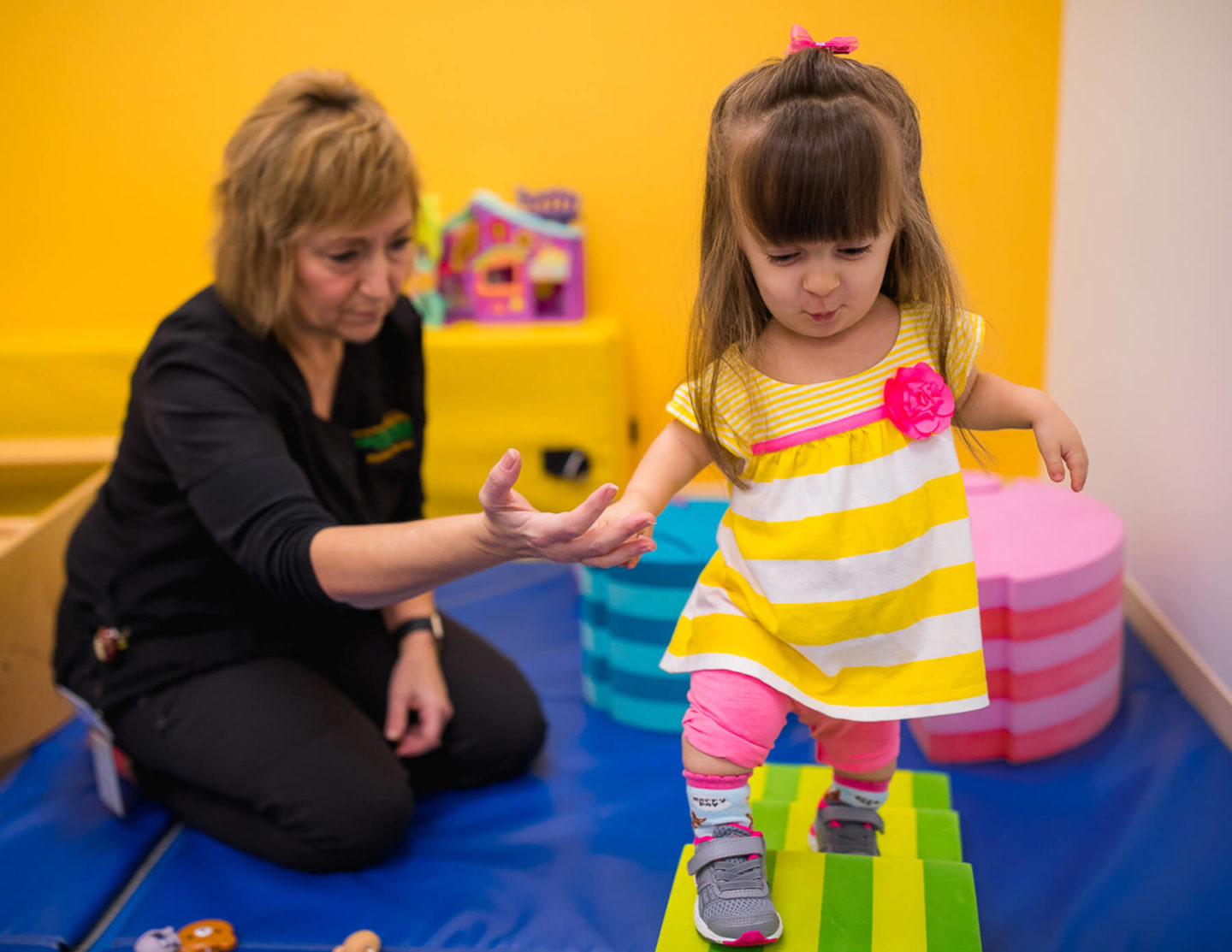 Evelyn practices balancing on colorful foam blocks with the help of a therapist.