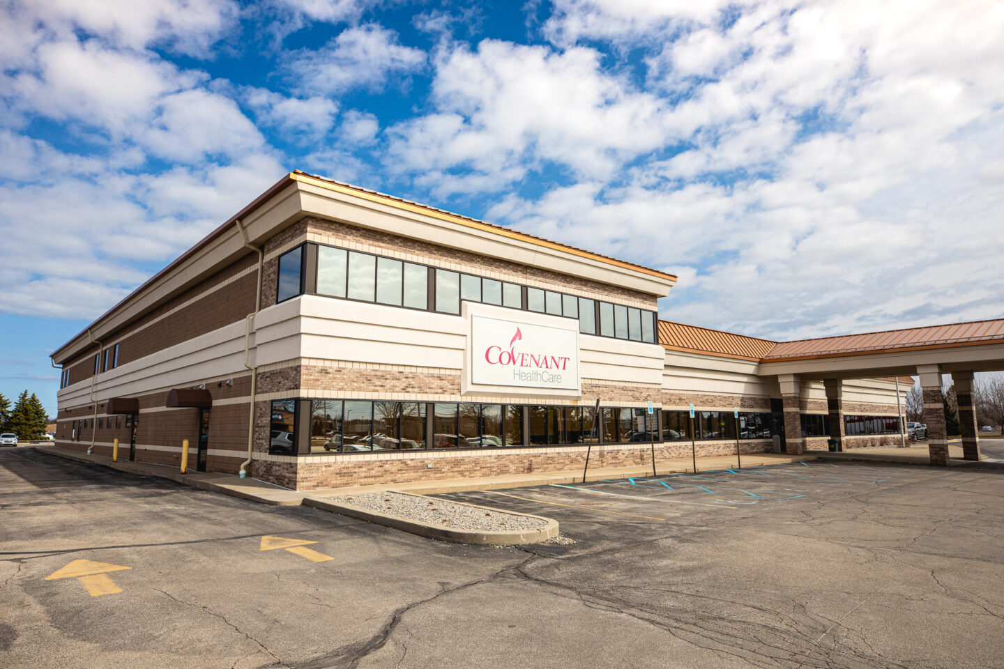 Exterior view of Mary Free Bed at Covenant HealthCare's outpatient therapy building under a bright blue sky, with an empty parking lot in the foreground.