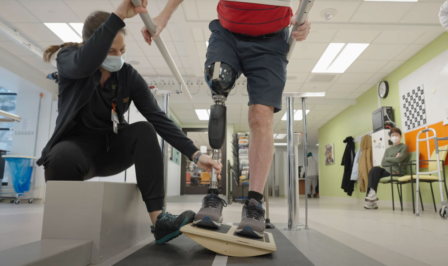 A patient with a prosthetic leg performs balance training with the assistance of a physical therapist.