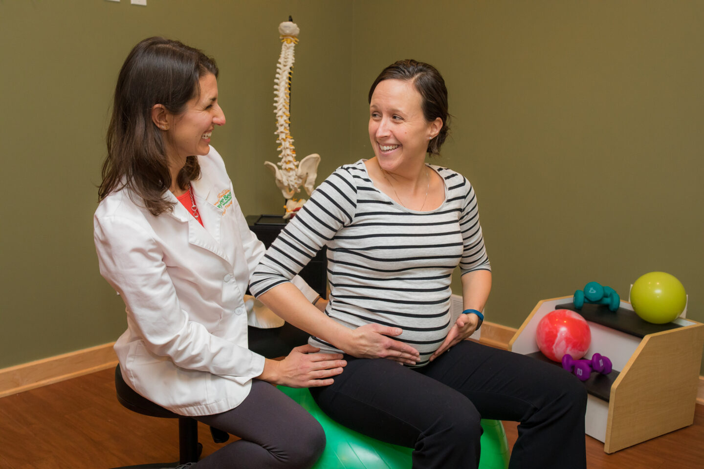 A physical therapist assists a pregnant woman with pelvic exercises on a stability ball.