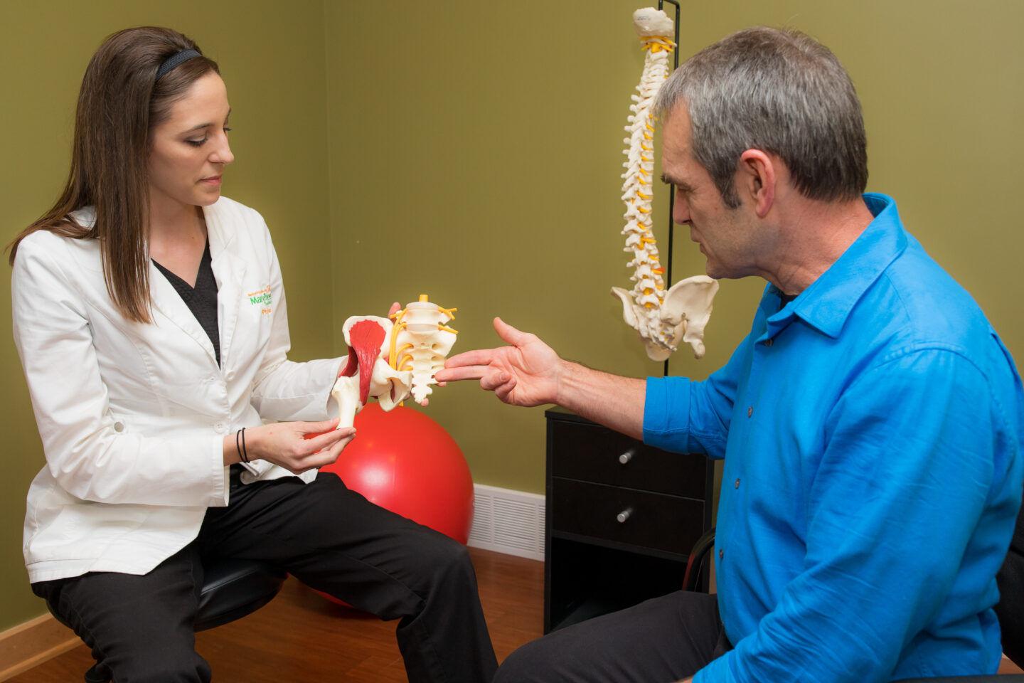A physical therapist explains pelvic anatomy using a model to a patient.