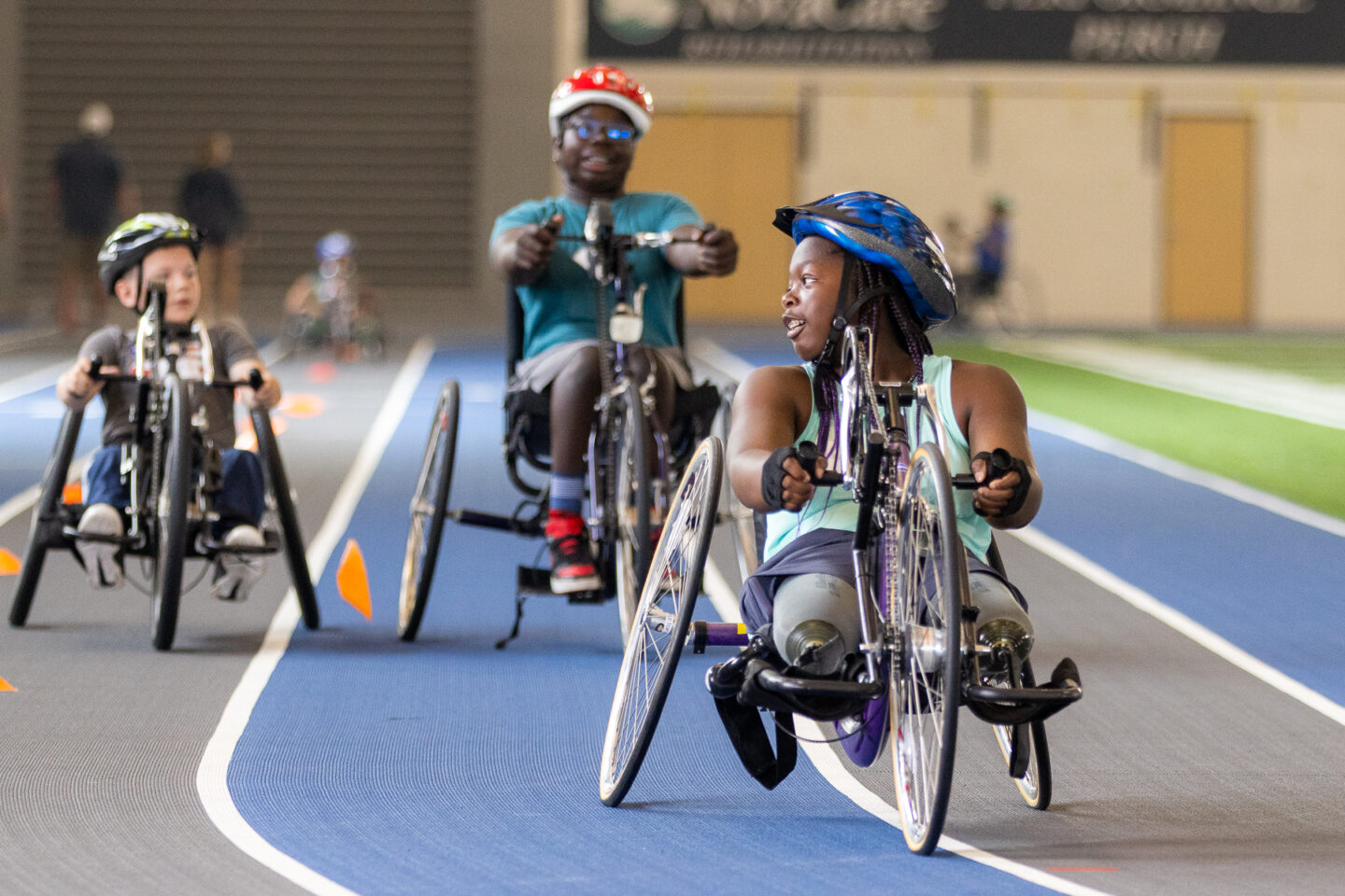 Participants riding handcycles on an indoor track.
