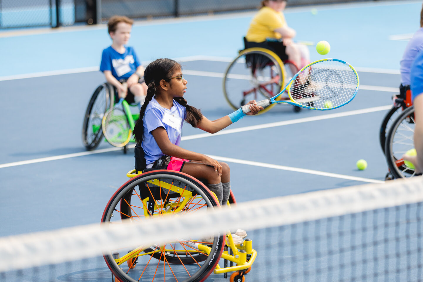 A young girl in a wheelchair practicing her tennis skills on a blue court.
