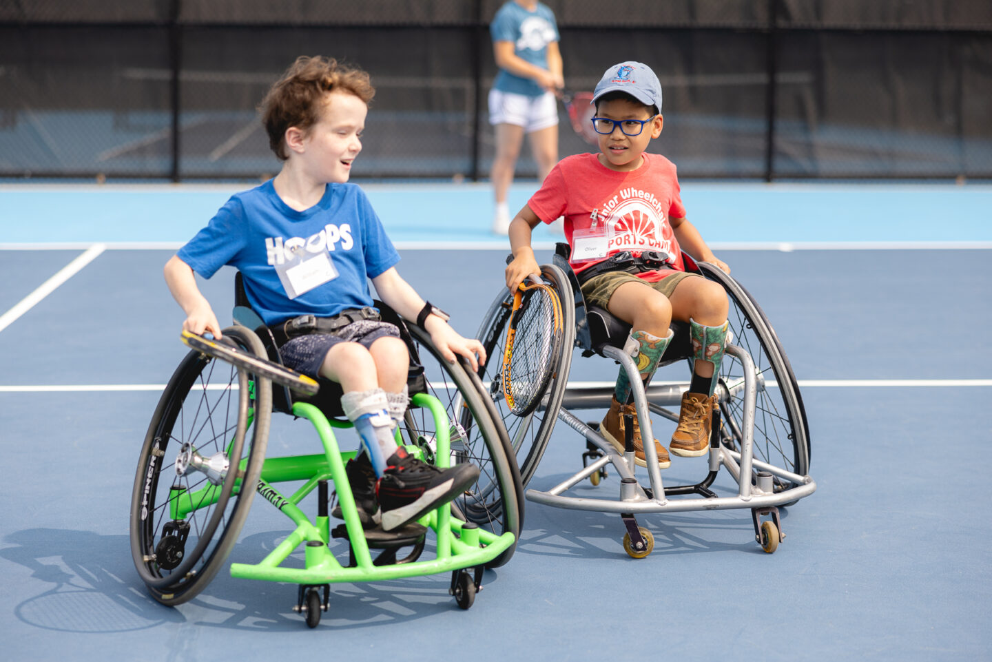 Two boys in wheelchairs playing tennis on a blue court.