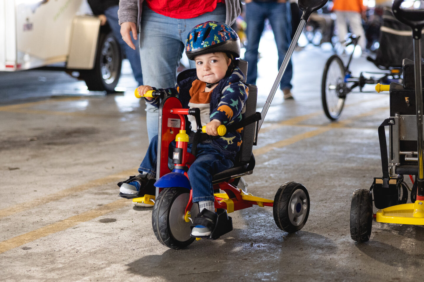 A young child wearing a helmet rides an adaptive tricycle at the Bikes for the Rest of Us event.