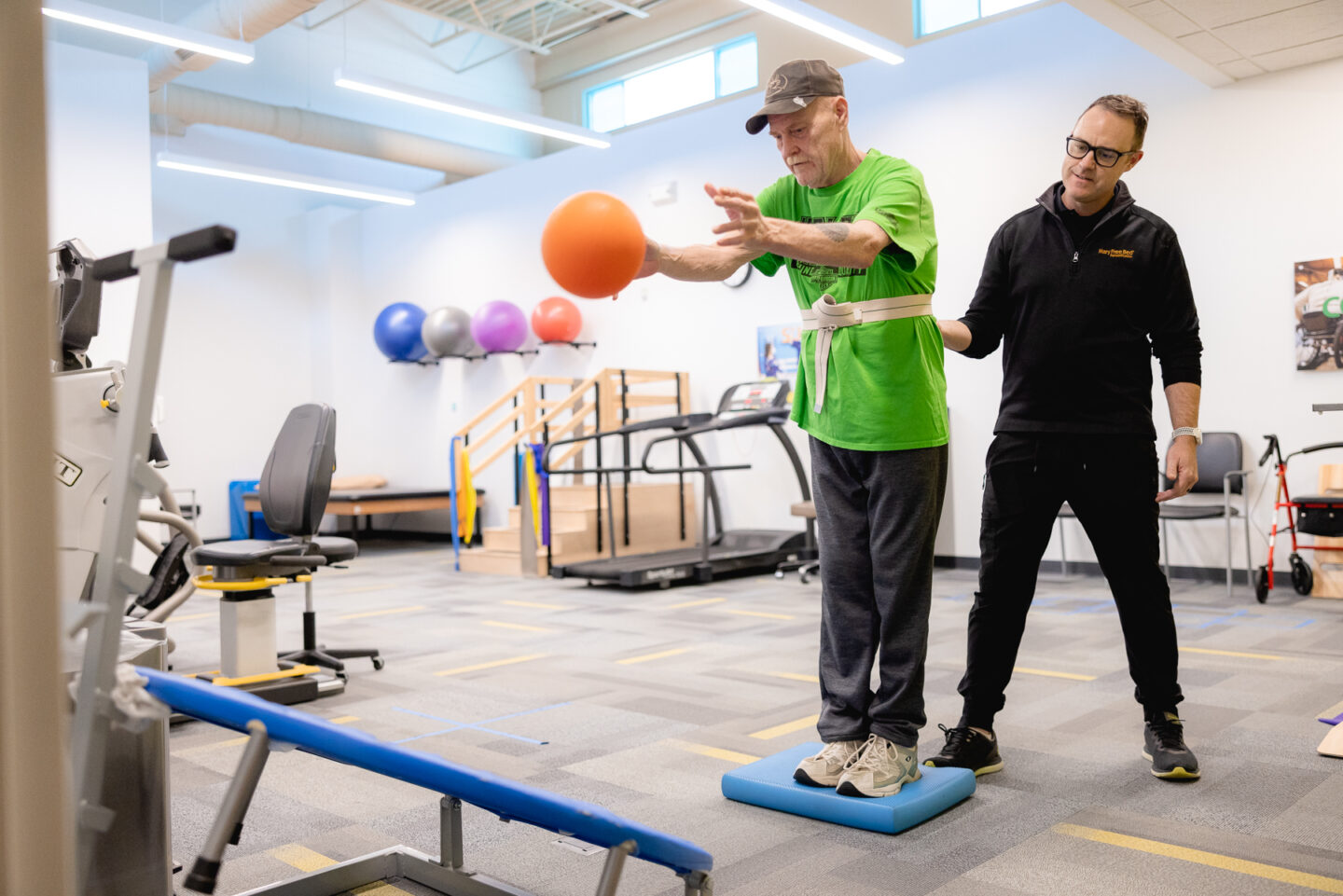 Physical therapist assisting older adult with balance exercise using a ball.