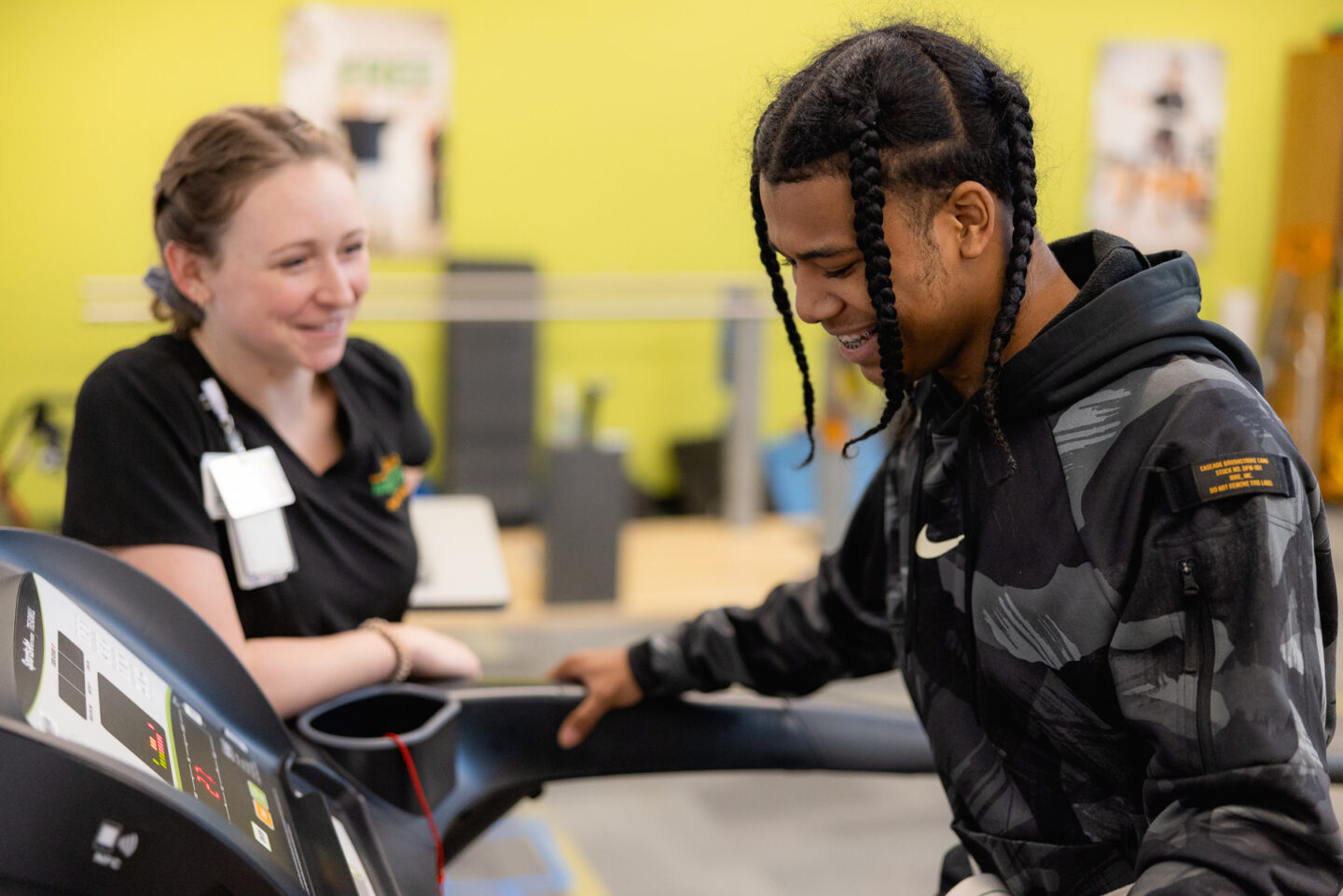 Physical therapist smiling while patient walks on a treadmill.