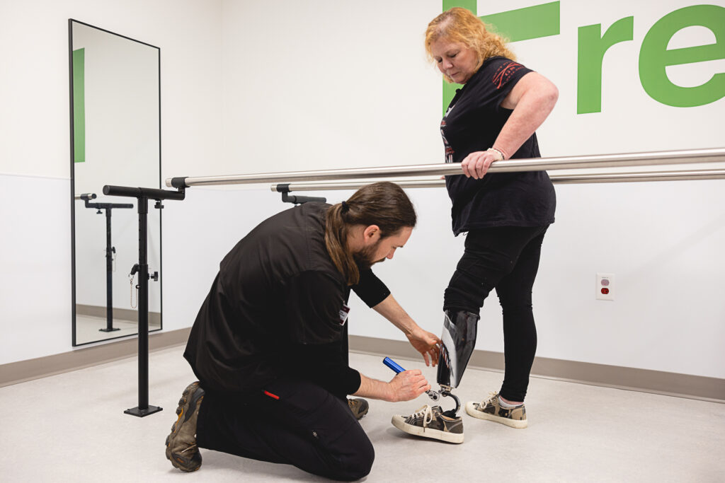 A certified prosthetist kneels to adjust a patient's prosthetic leg during a fitting session.