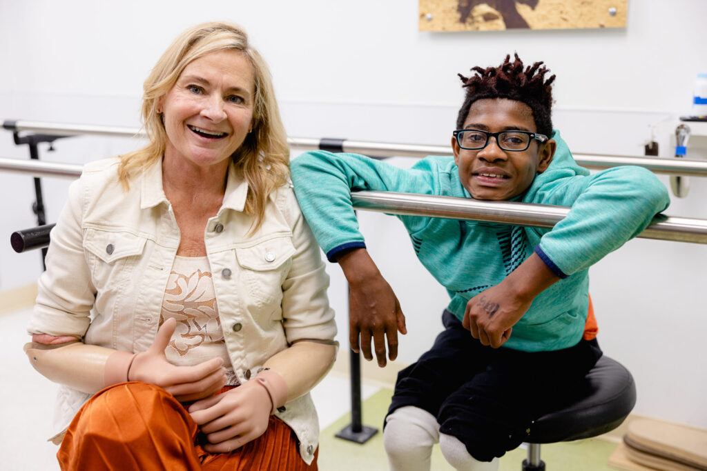A woman with prosthetic arms and a boy with prosthetic legs smile together.