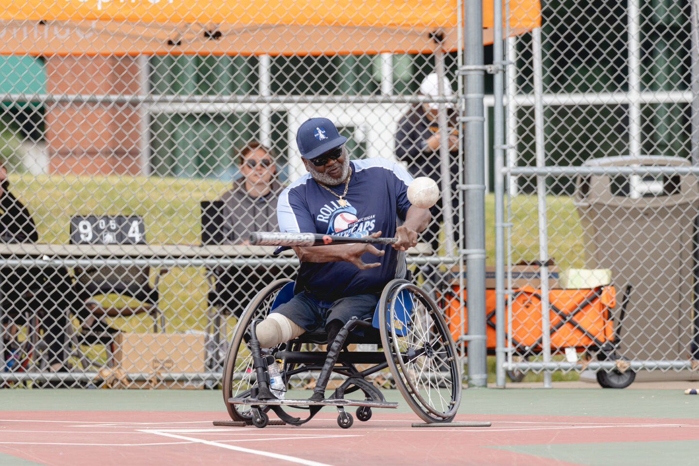 A wheelchair softball player taking a swing at the ball during an adaptive sports tournament.