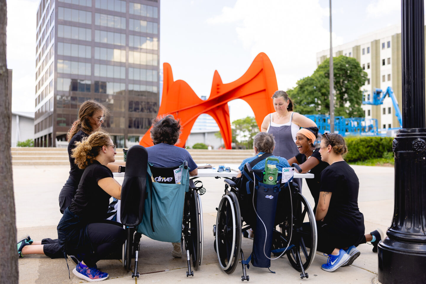 Group of people in wheelchairs and caregivers engaging in art therapy outside at Calder Plaza.