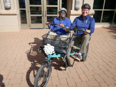 Tandem Bike with two individual sitting on it at ribbon cutting