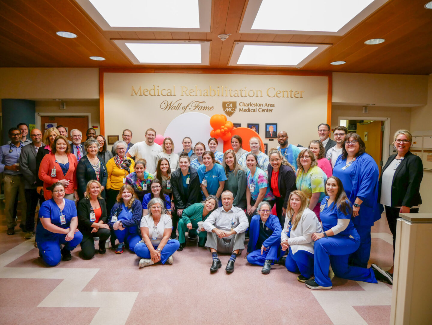 Hospital staff including nurses, therapists and administrators posing for a photo smiling and sitting in a group