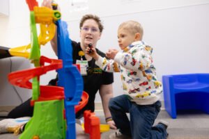 Speech-language pathologist conducting therapy with a toddler using colorful stacking and building toys, encouraging communication and developmental skills in a clinical therapy setting